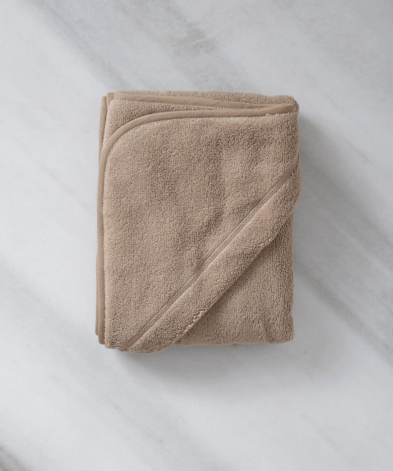 Folded Baby Hooded Towel in color latte, flat lay shot with marble background