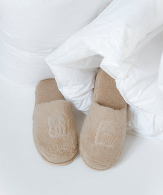 bathslippers in color latte with DOUXE logo, laying in a duvet