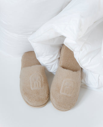 bathslippers in color latte with DOUXE logo, laying in a duvet